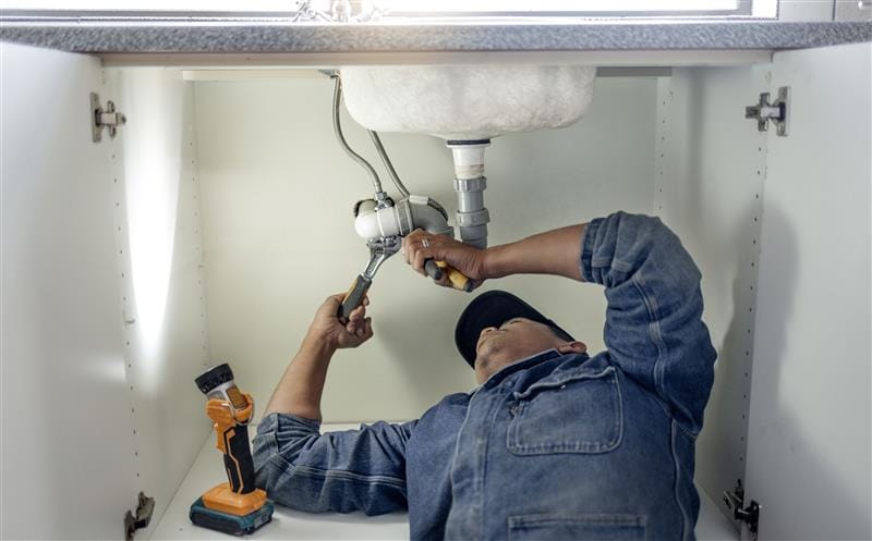 Plumber repairing pipes beneath a bathroom sink in Olivehurst